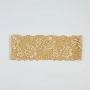 Nahaufnahme von champagnergoldener elastischer Spitzenborte, zartes florales Blumenmuster.