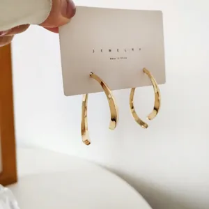 Detailed close-up view of fashionable metal curved C-shaped hoop earrings on display card.