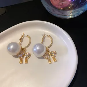 Close-up detail of elegant gold hoop earrings featuring large pearls and sparkling bow pendants.