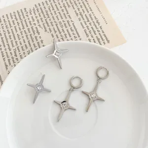 Close-up detail of silver four-pointed star cross earrings with sparkling central zircon.