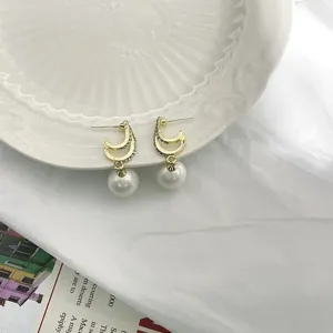 Nahaufnahme eleganter c-förmiger Strass-Perlen-Ohrringe mit glänzenden hängenden weißen Perlen.