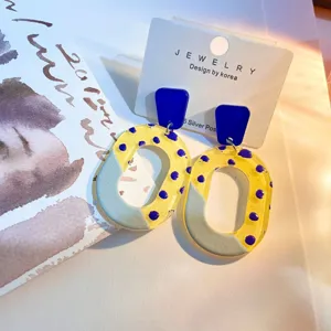 Nahaufnahme der geometrischen Acryl-Ohrringe mit blauem Oberteil und gelb-lila gemustertem Ring.
