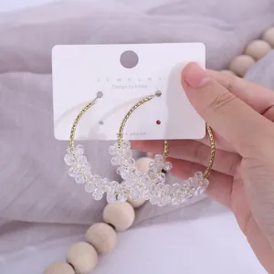 Gros plan de boucles d'oreilles créoles en perles de cristal avec fil doré sur carton blanc.