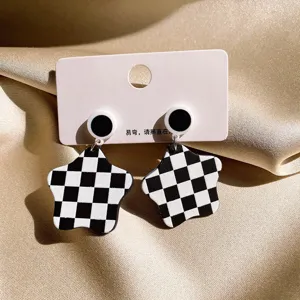 Detailed shot of black and white checkerboard star earrings on white hanging card display.