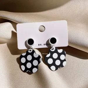 Close-up detail of black and white polka dot flower earrings on display card with satin background.