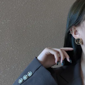 Detail shot of retro round leopard print earrings with twisted metal border worn on ear.
