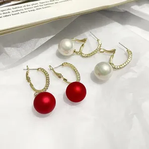 Close-up detail of C-shaped gold hoop earrings with white pearls and red beads on white paper.
