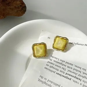 Nahaufnahme von quadratischen gelben Ohrringen mit strukturiertem goldenem Metallrahmen.