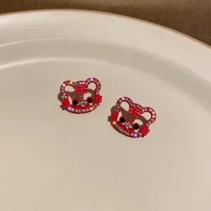 Close-up of red rhinestone tiger stud earrings, sparkling crystal details on clean white plate.