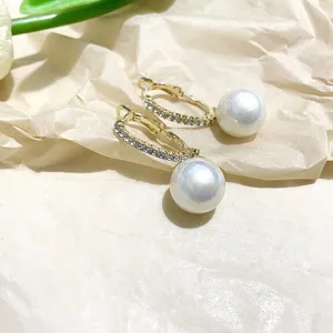 Detail view of C-shaped pearl hoop earrings with shiny rhinestones and a dangling white pearl charm.