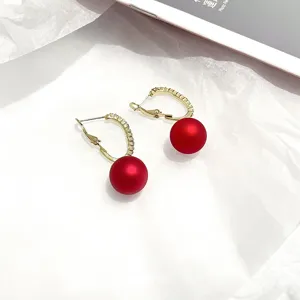 Gold-tone C-shaped hoop earrings with red matte pearl drop, exquisite jewelry detail view.