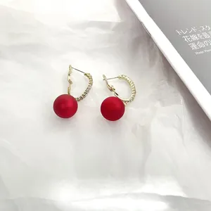 Close-up detail of C-shaped rhinestone and red pearl hoop earrings with silver needle.