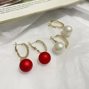 Detail view of trendy C-shaped hoop earrings featuring elegant red and white pearl pendants.