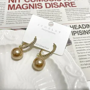 Gold C-shaped rhinestone pave hoop earrings with dangling champagne pearl charms for women.