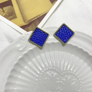 Close-up of square blue textured earrings with elegant twisted metal rope rims on a ceramic tray.
