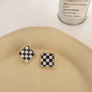 Detailed shot of black and white checkerboard square earrings with golden twisted metal edge.