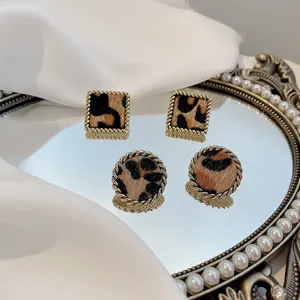 Close-up of retro leopard print earrings with gold twist border on vintage mirror tray.