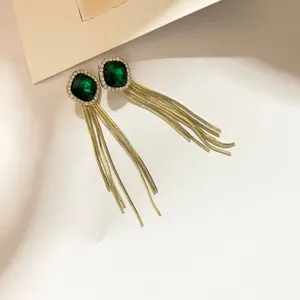 Vue détaillée de boucles d'oreilles longues à franges dorées élégantes avec pierre verte et strass.