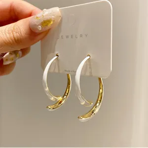 Detail view of minimalist gold and white curved hoop earrings on a presentation card.