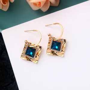 Close-up of gold geometric square earrings with sparkling blue crystals and rhinestone pave.