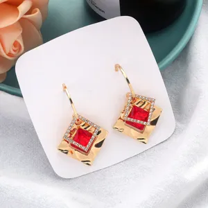 Detailed view of gold geometric square earrings featuring sparkling red crystals and rhinestones.