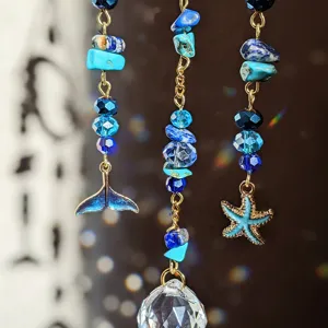 Blue crystal suncatcher detail with starfish and whale tail pendants, romantic rainbow light.