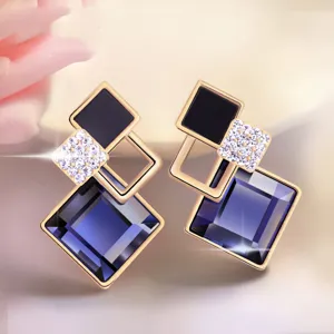 Close-up van geometrische strass oorbellen met blauwe vierkante kristallen en zwarte inleg.