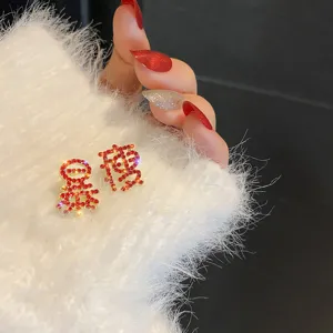 Gedetailleerde close-up van asymmetrische strass oorbellen met Chinese karakters op witte stof.