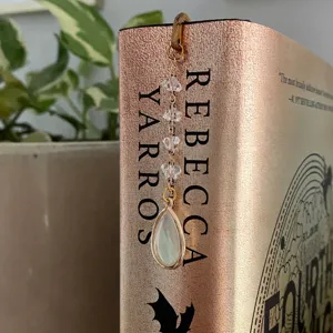 Metal hook bookmark detail featuring crystal beads and a teardrop pendant on a book.