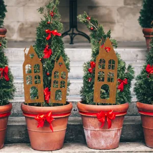 Metal rusty house silhouette garden stakes detail shot with potted green plants and red bows.