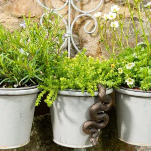 Detail view of a charming bronze snake planter companion decorating a garden flower pot.