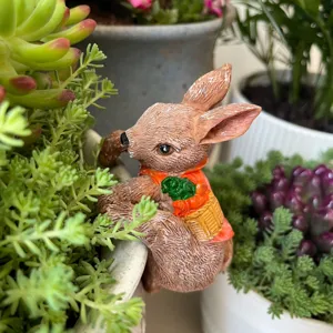 Detalle de lindo conejito de resina colgado en el borde de maceta con cesta de zanahorias.