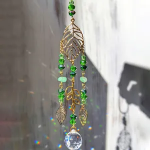 Gros plan sur le pendentif en feuille de cristal suspendu avec des perles vertes et des reflets.