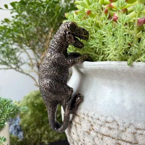 Gros plan détail d'un cintre de pot de fleurs dinosaure T-Rex en résine sur un pot en céramique.