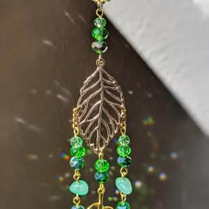 Vue rapprochée du pendentif feuille creuse dorée avec des perles de cristal vert et des pierres.