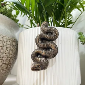 Detailed close-up shot of a bronze snake pot hanger clinging to a white ribbed planter.