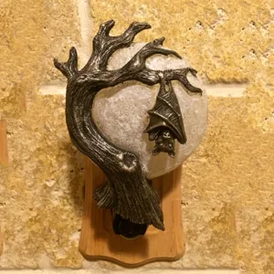 Detail shot of Halloween bat night light featuring tree branch and moon design plugged into wall.