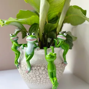 Close-up of cute resin green frog hanging figurines on flower pot, ideal for garden plant decor detail.