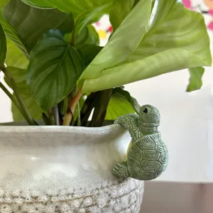 Resin turtle pot hanger detail, cute garden decoration hanging on ceramic flowerpot edge.