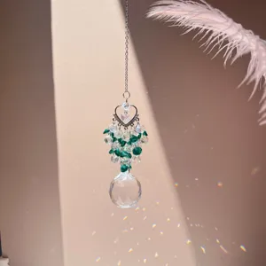 Close-up detail of hanging crystal suncatcher prism with heart top and green beads in sunlight.
