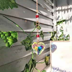 Detailed shot of an iridescent crystal heart suncatcher hanging ornament with gold chain and beads.