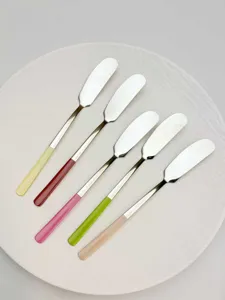 Close-up view of stainless steel butter knives set with colorful handles neatly arranged on a white plate.