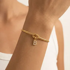 Dettaglio in primo piano del bracciale a catena di serpente dorato con ciondolo lettera B.
