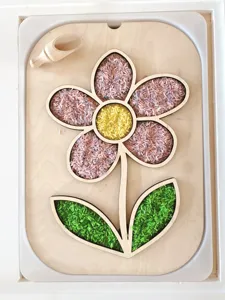 Bandeja sensorial de madera con forma de flor, arroz de colores y pequeña cuchara.