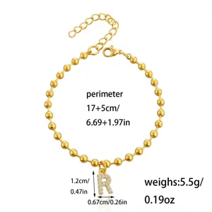 Dettaglio del bracciale di perle dorate con ciondolo a lettera R in strass scintillante e catena.