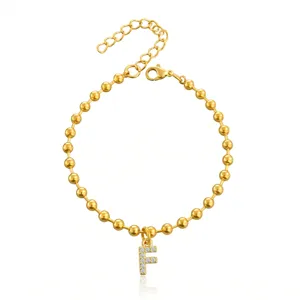 Dettaglio del bracciale di perle dorate con ciondolo lettera F tempestato di cristalli.