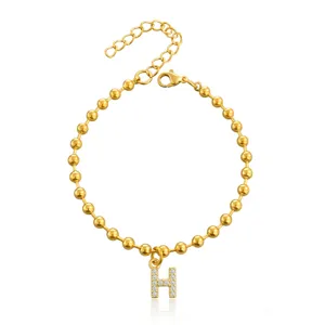 Primo piano del bracciale con catena a sfere dorata con pendente a lettera H pavé di cristalli luminosi.