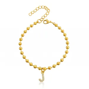 Dettaglio di bracciale di perle dorate con ciondolo a lettera J in strass luminosi.