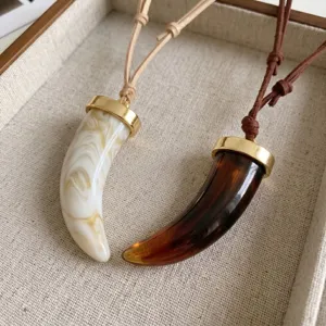 Gros plan détaillé de colliers pendentifs dent de loup tendance avec cordons en suédine réglables.