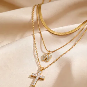 Gros plan d'un élégant collier doré à trois couches avec pendentif lettre W et croix.